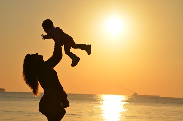 A mother holding her child up on the beach at sunset